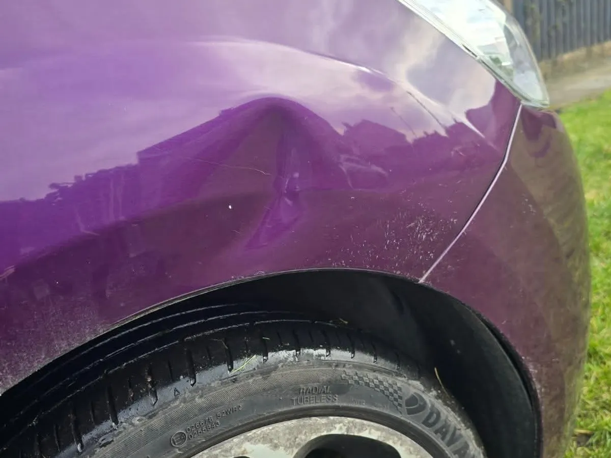 The front wing of a purple Citroen with a crease pushed into the panel above the wheel arch.