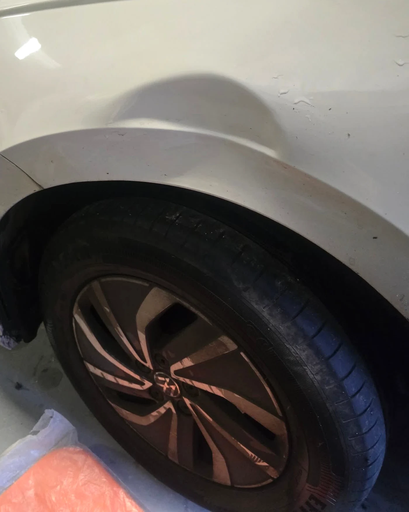The front wing of a white car with a dent dished into the panel above the wheel arch.