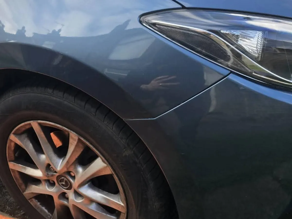 The same dark blue wing after repair, with the paintless repair mat and rods still on the ground beside the wheel.
