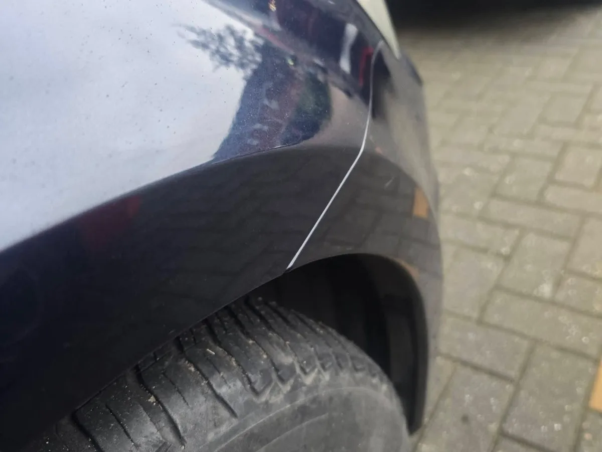 The same dark blue quarter panel after repair, the body line running straight and unbroken down to the wheel arch.